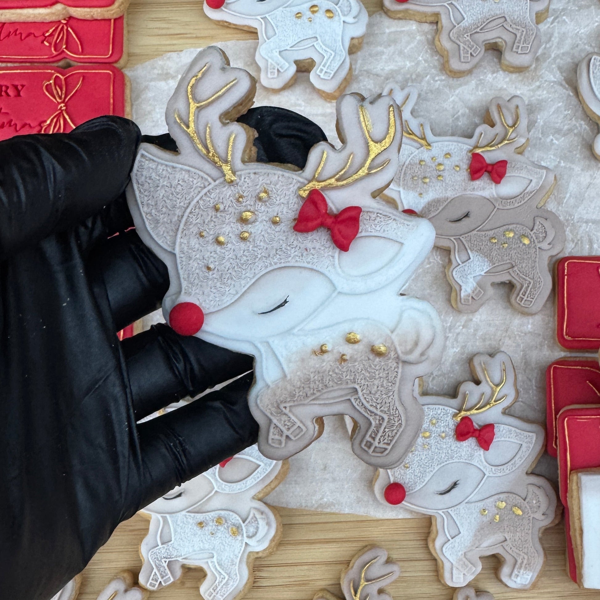 Decorative cookies shaped like reindeer with red bows, held by a gloved hand against a wooden background.